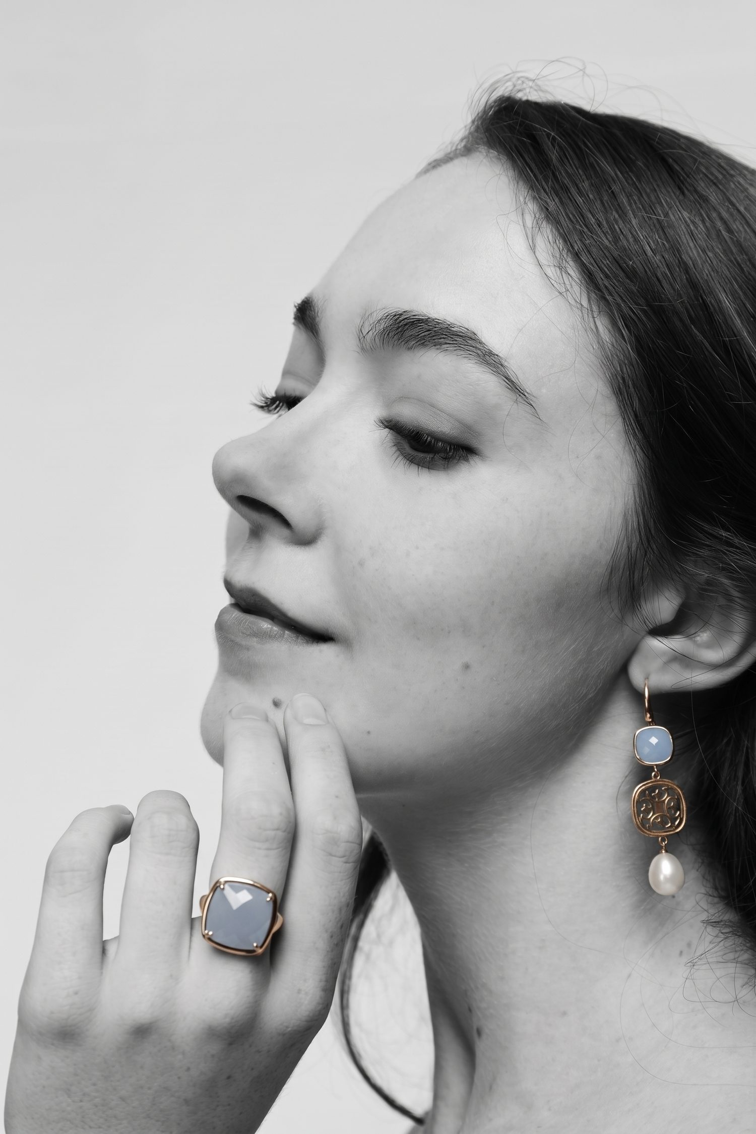 A black and white portrait in which only the blue stones of the earrings and ring carry colour