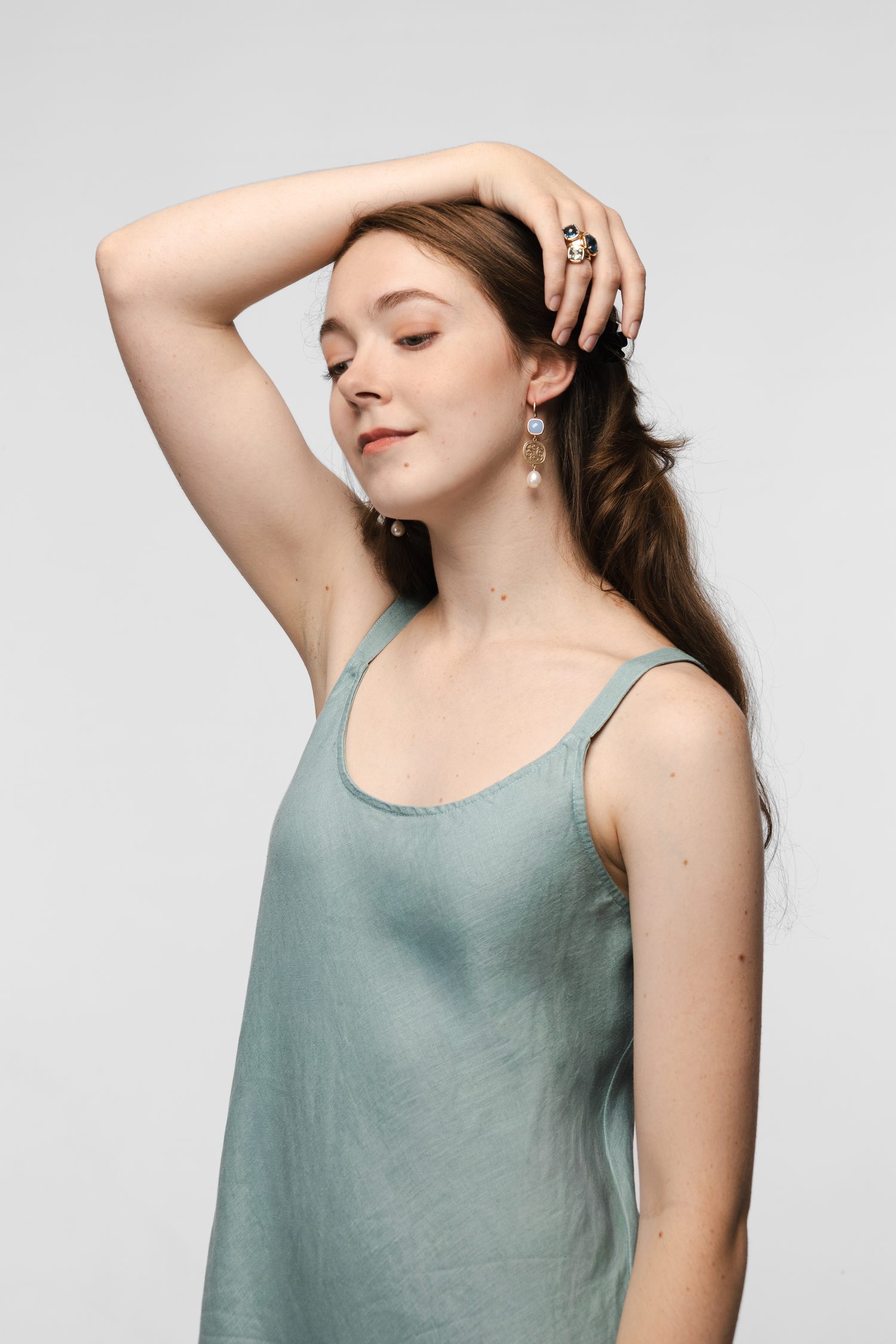 A woman wearing drop earrings set with a pale blue stone above a pearl