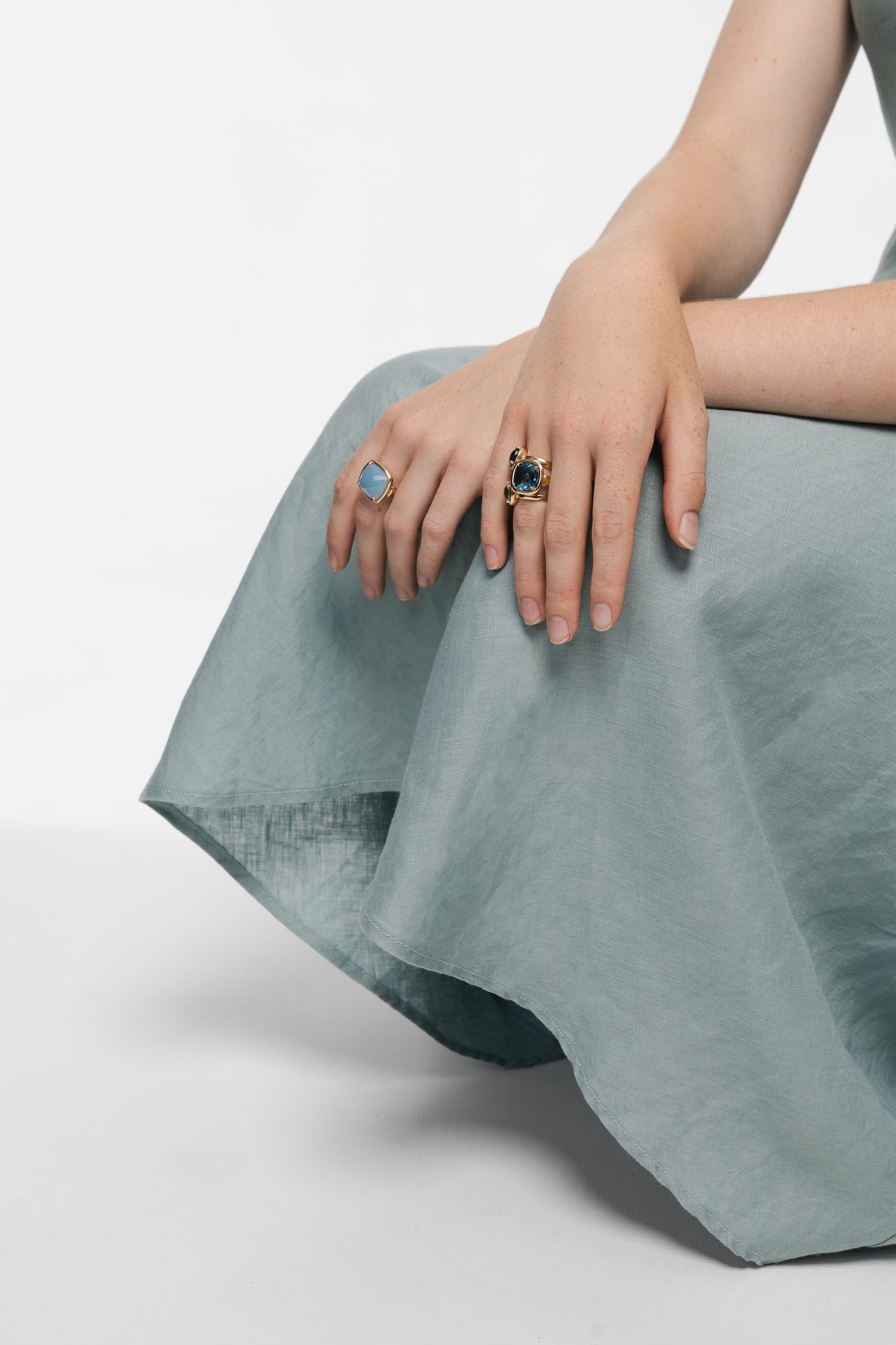 Two rings set with blue stones, worn on hands resting on sage linen