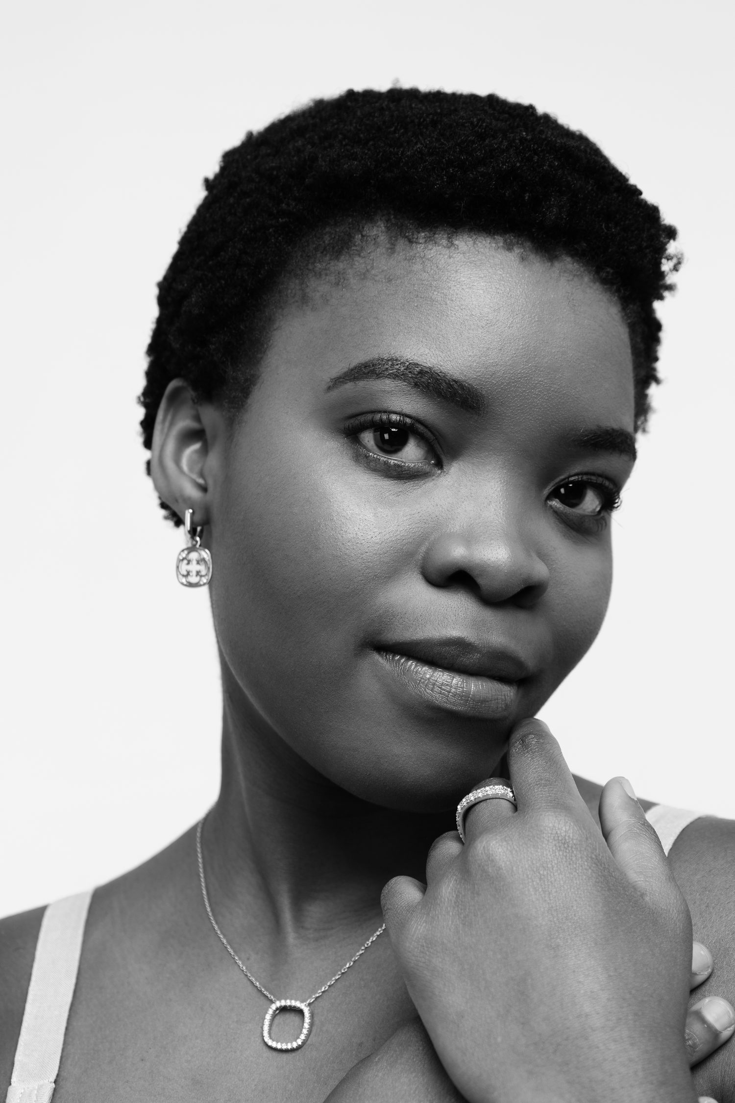 A woman wearing an open-square pendant, pavé ring and drop earring, photographed in black and white